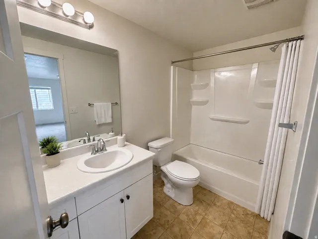 Full downstairs bathroom featuring a white vanity with an integrated sink, a large wall-mounted mirror, overhead vanity lighting, a full tub with shower surround, and tiled flooring