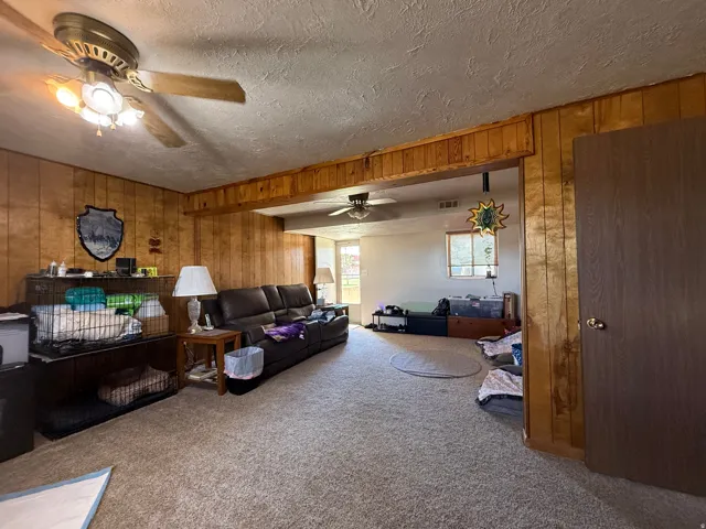 Carpeted flooring, wood-paneled walls, ceiling fan with integrated lighting, and a doorway