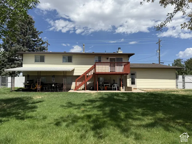 Two-story residence with light-colored siding, a second-story deck, and an expansive ground-level patio with a full-length awning