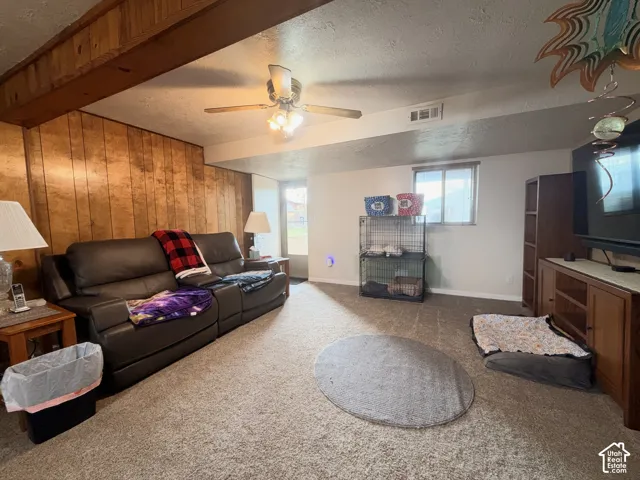 Interior space featuring wood-paneled accent wall, exposed ceiling beam, neutral wall-to-wall carpeting, and a central ceiling fan with integrated lighting