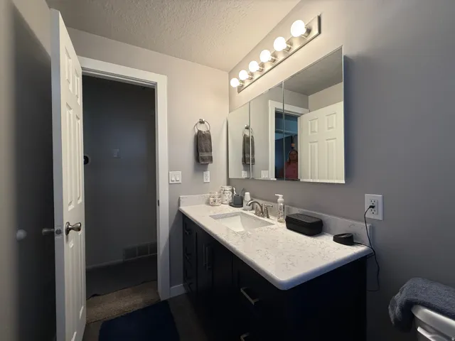 Vanity with white countertop, undermount sink, and dark cabinetry