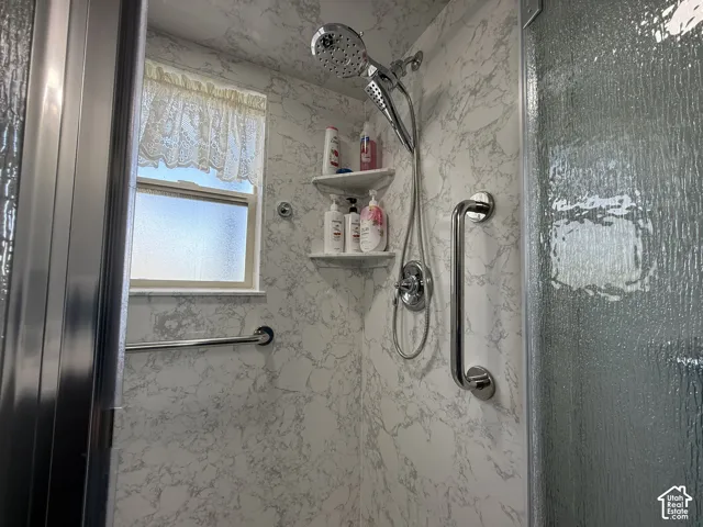 Shower enclosure with marbling wall panels, a multi-function shower head, built-in shelving, and grab bars