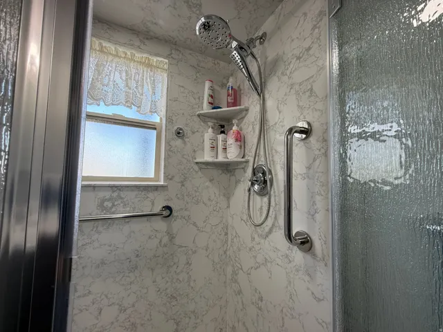 Shower enclosure with marbling wall panels, a multi-function shower head, built-in shelving, and grab bars
