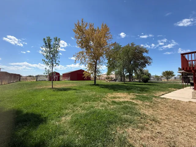 Expansive grassy yard with mature trees, a red barn, and an additional red storage shed