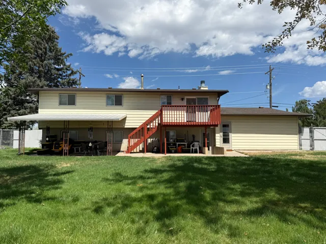 Two-story residence with light-colored siding, a second-story deck, and an expansive ground-level patio with a full-length awning