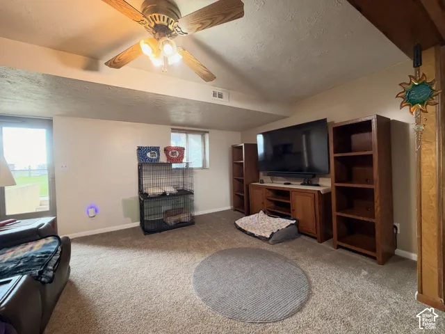 Room featuring neutral wall-to-wall carpeting, vaulted ceiling, built-in wooden media cabinetry with integrated shelving, and a ceiling fan with light fixture