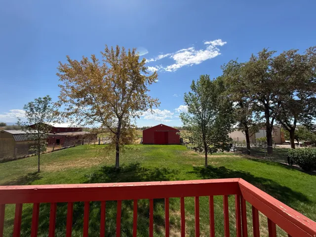 Expansive outdoor space featuring a red wooden railing, a verdant lawn, mature trees, and a red barn structure