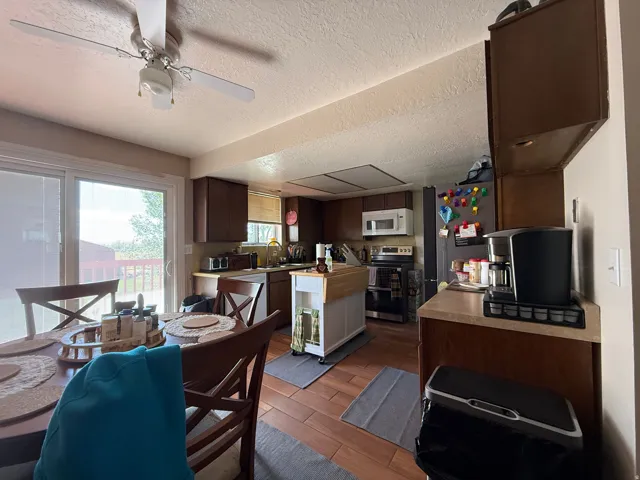 Wood-finish flooring, dark wood cabinetry, and a ceiling fan with integrated lighting