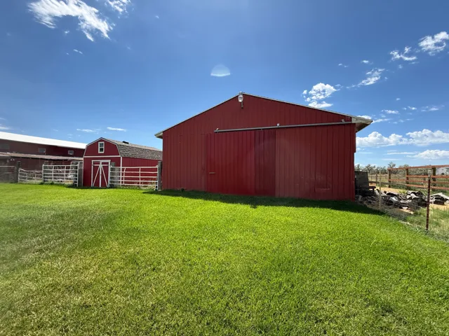 Expansive green lawn with red outbuildings, a red barn with a sliding door, and white fencing