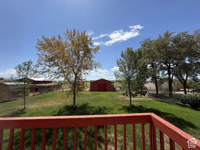 Expansive outdoor space featuring a red wooden railing, a verdant lawn, mature trees, and a red barn structure