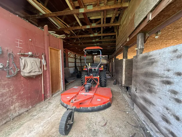 Wood-frame barn interior featuring exposed rafters, wood slat walls, and a dirt floor