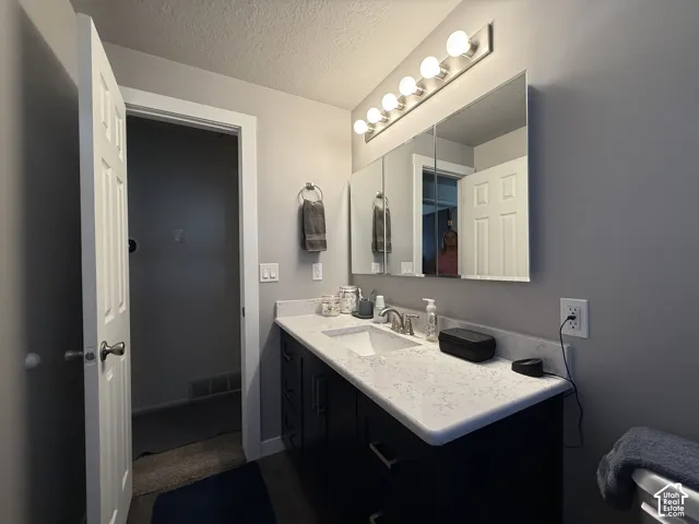 Vanity with white countertop, undermount sink, and dark cabinetry