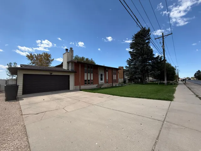 Exterior featuring a prominent attached garage with a dark panel door, a concrete driveway, and a front lawn with mature trees