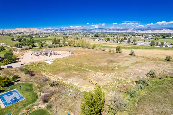Expansive land parcel featuring a partially constructed residence, surrounding mountainous terrain, and distant residential structures