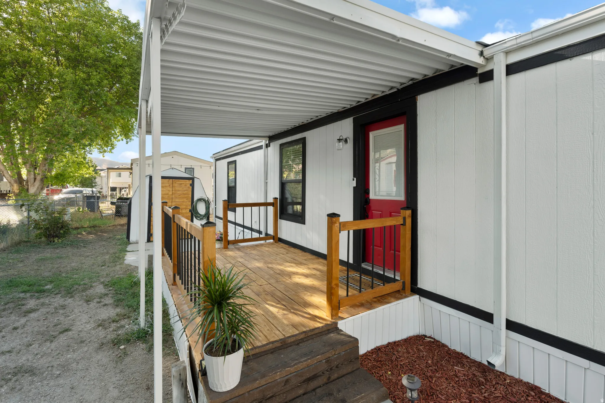 Expansive covered wood-finish deck with black metal and wood railings, featuring a vibrant red entry door