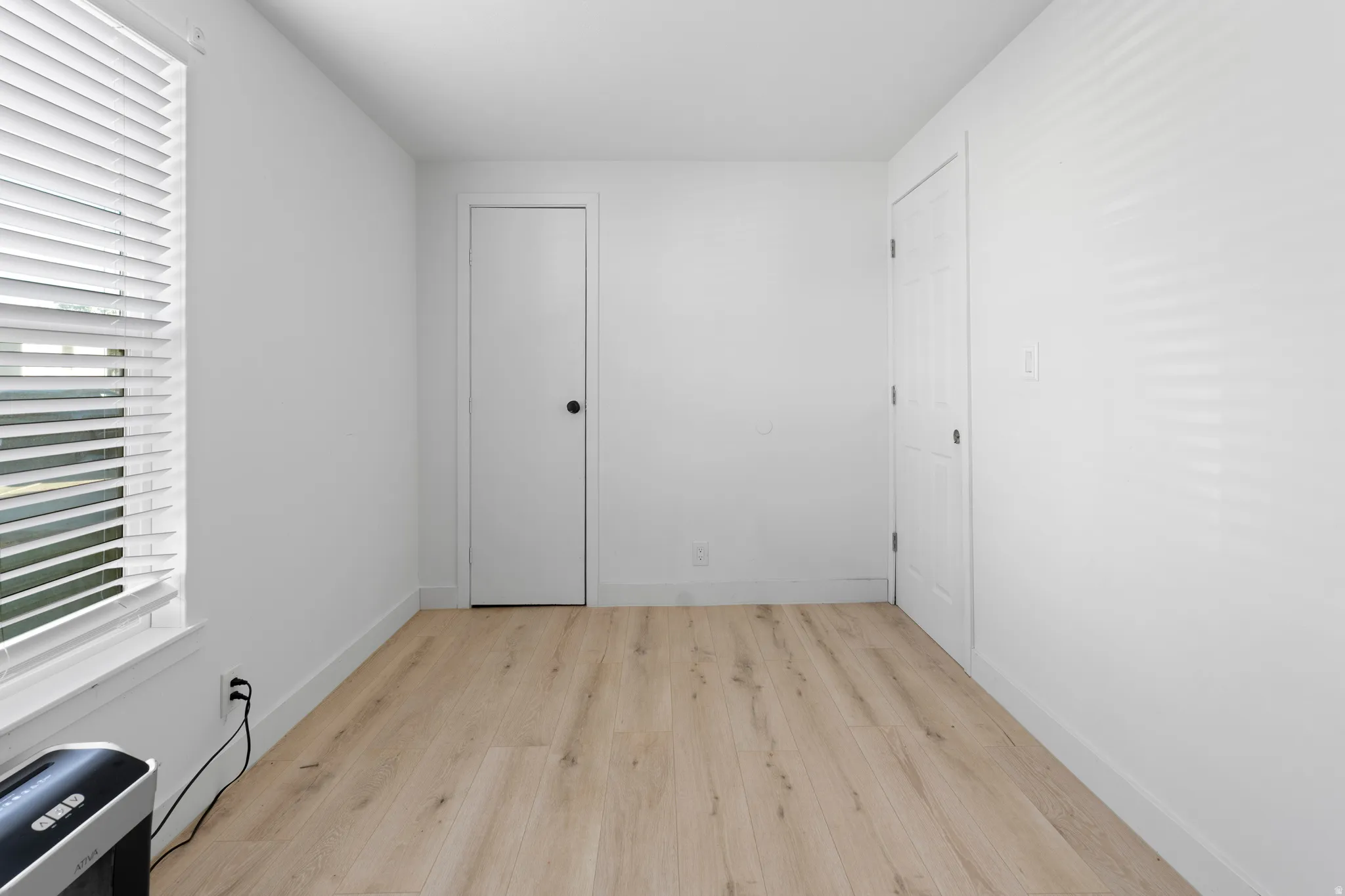 Wood-finish flooring with crisp white walls, a window with horizontal blinds, and two solid panel doors