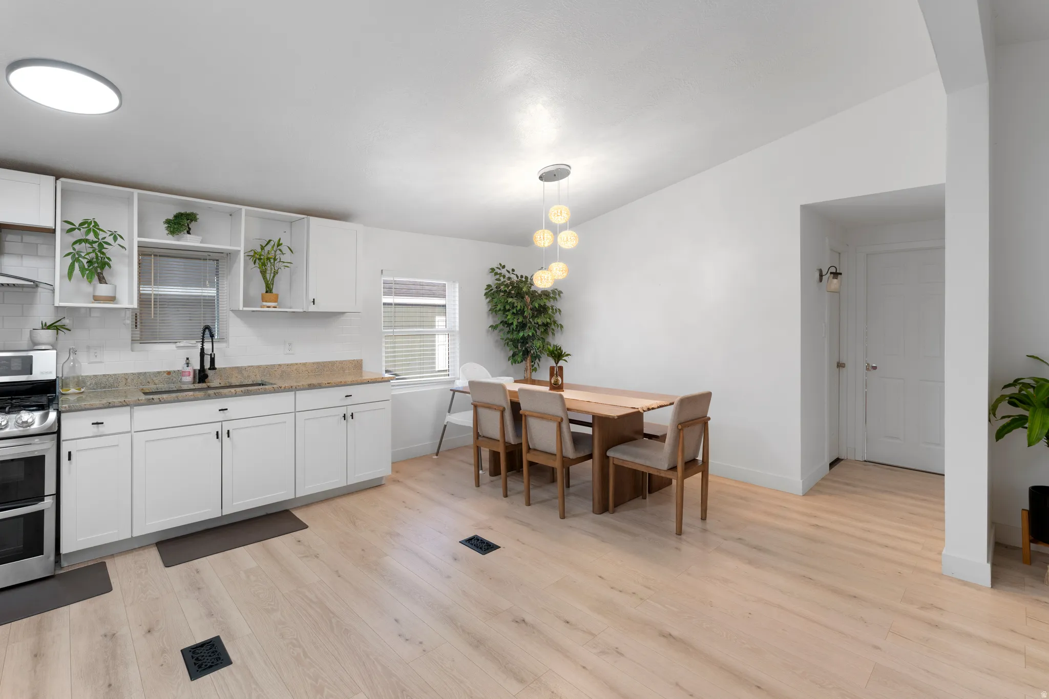 Light wood-finish flooring, white cabinetry, granite-style countertops, stainless steel appliances, and a modern dining light fixture