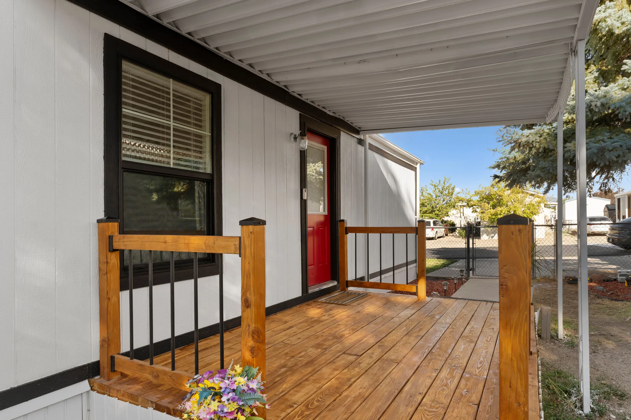 Covered porch featuring wood flooring, wood railing with metal balusters, and a red entry door