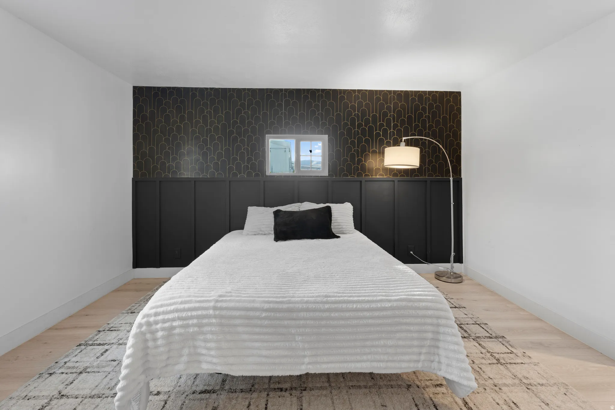 Light wood-finish flooring, a decorative accent wall with black paneling and patterned wallpaper, and a rectangular window