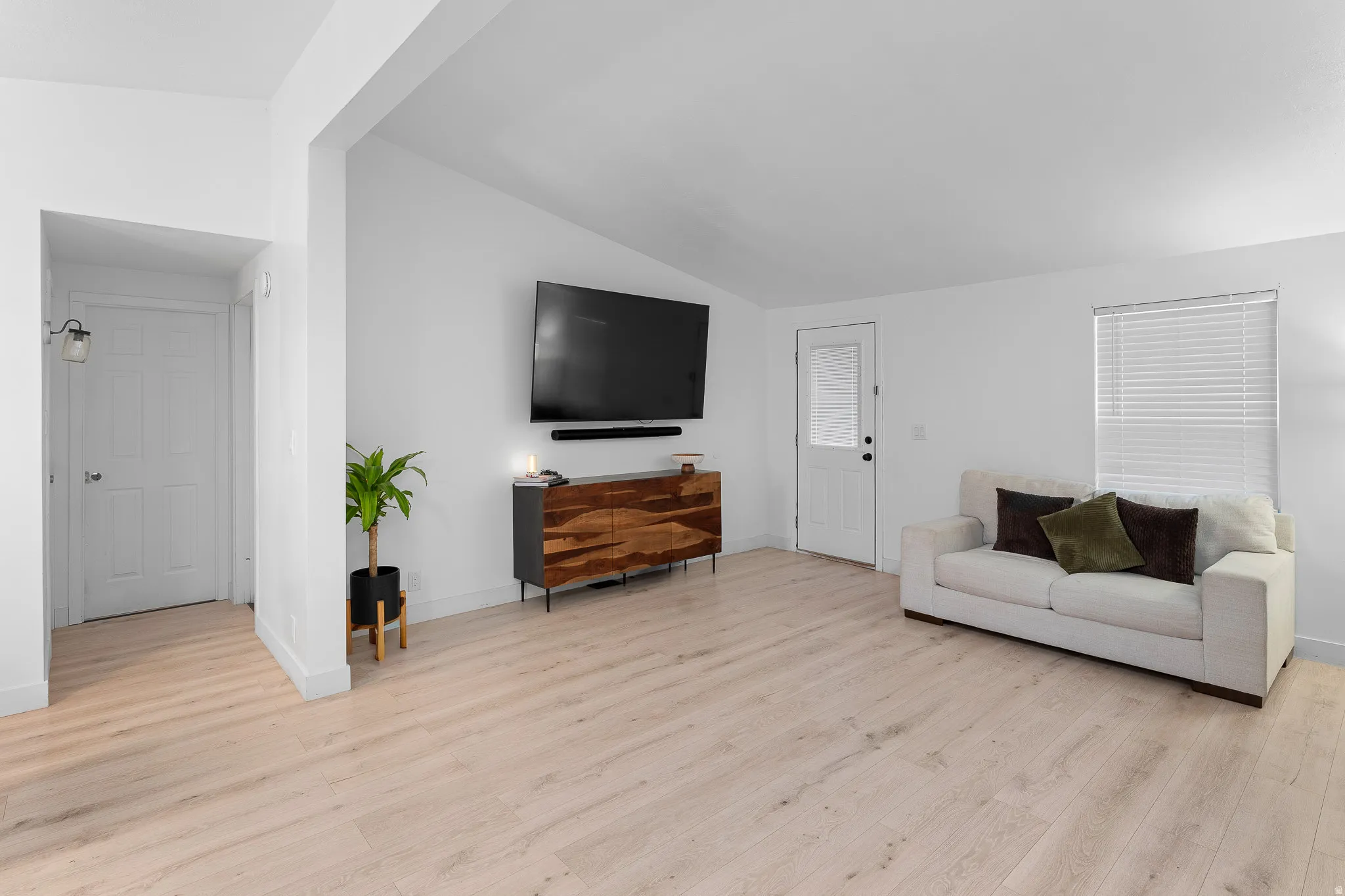 Light wood-finish flooring with white walls and a large window with blinds
