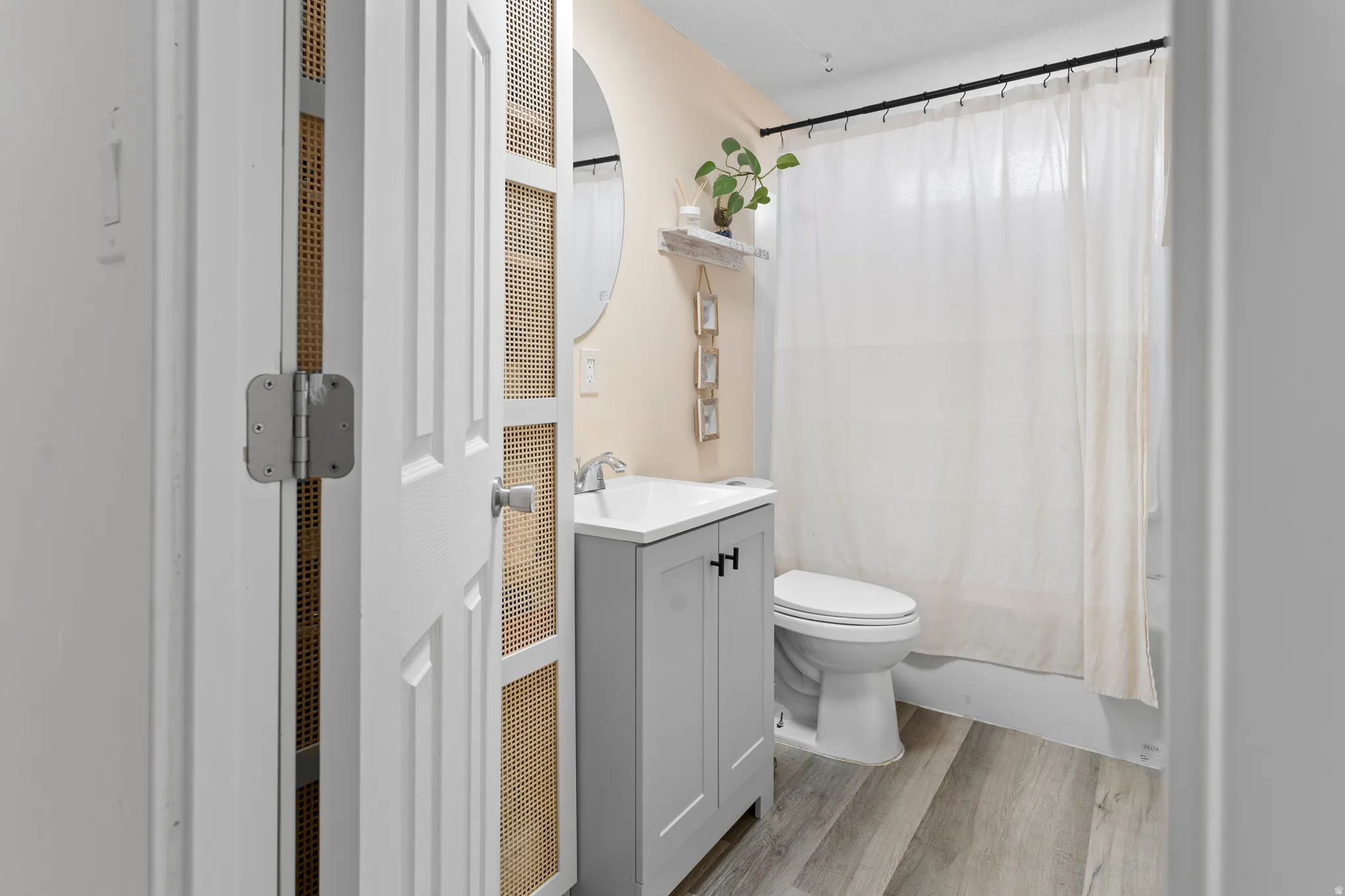 Wood-finish flooring, white vanity with black hardware, round mirror, and a built-in bathtub with shower