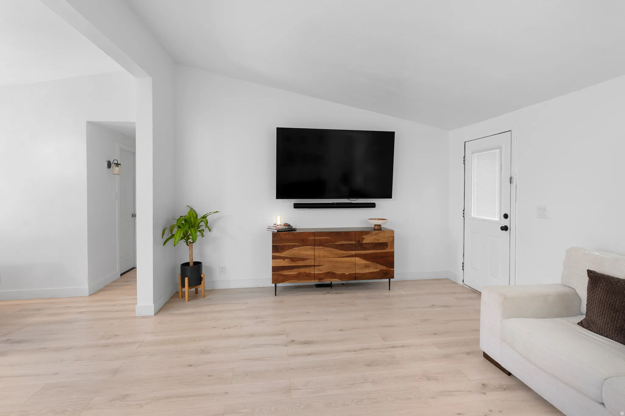 Light wood-finish flooring, white walls, and a white entry door with a frosted pane