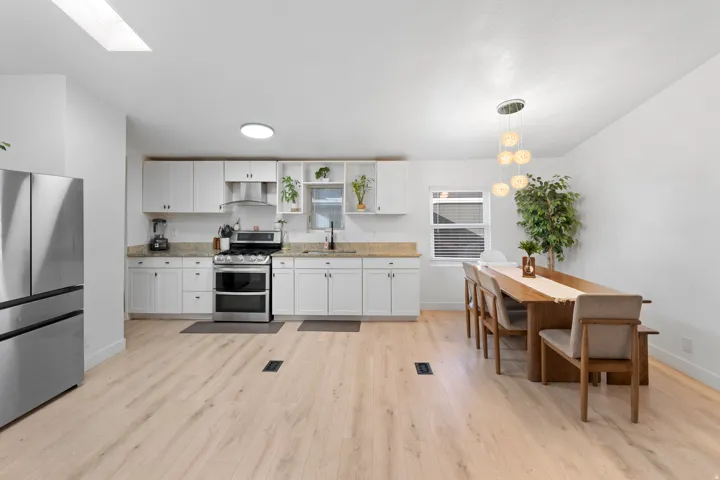 Bright kitchen with white cabinetry, stainless steel appliances, stone countertops, and wood-finish flooring