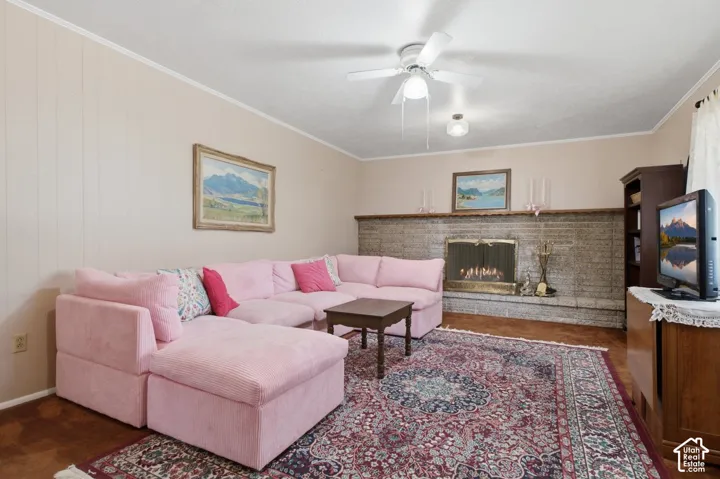 Stone-faced fireplace with a metal insert, ceiling fan with integrated lighting, textured wall paneling, and an exposed wood-finish flooring border