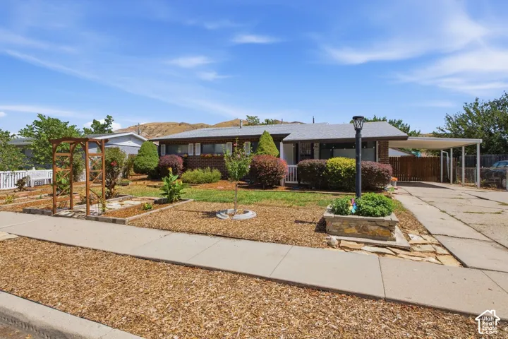 Brick exterior with a covered carport, established landscaping, and a front yard with a wooden arbor