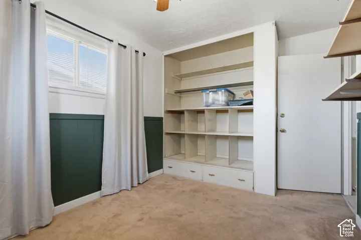 Built-in shelving with integrated drawers, neutral carpet flooring, and a single window with blinds