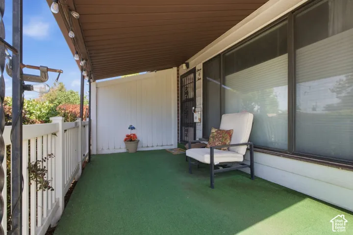 Covered porch with green outdoor carpeting, white railing, and decorative security screen door