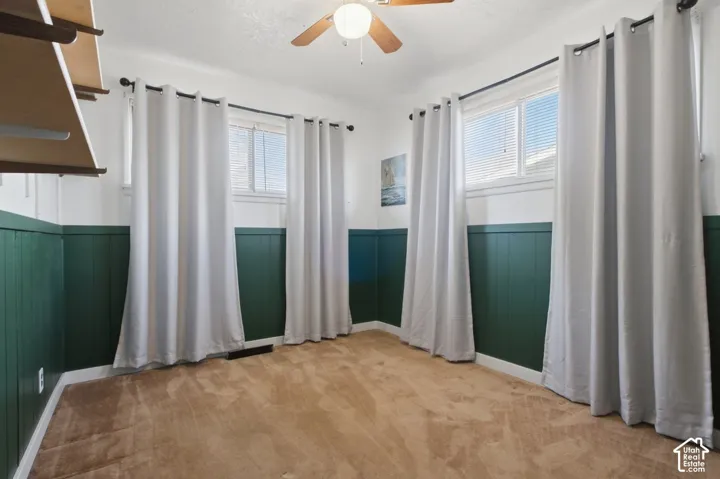Light-colored carpeting, two windows with blinds, and a built-in ceiling fan with light fixture