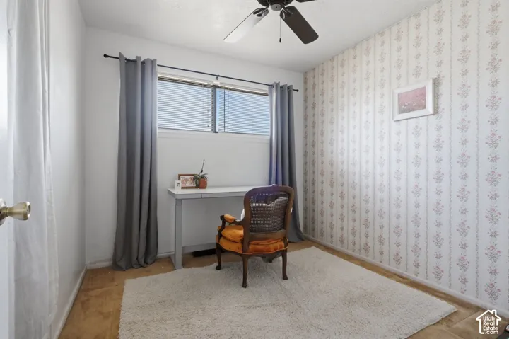 Wood-finish flooring, overhead ceiling fan, window with blinds, and patterned wallpaper
