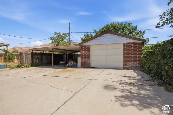 Attached brick garage with a single vehicle door and a covered carport with metal supports, concrete driveway