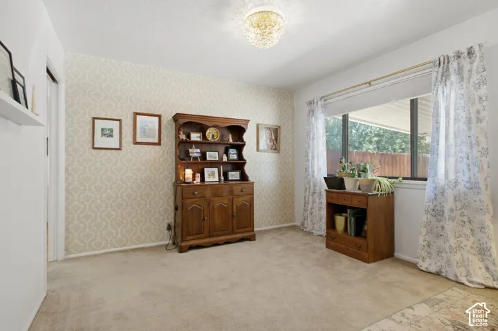 Patterned wallpaper accent wall, neutral carpeting, large window, and a decorative ceiling light fixture
