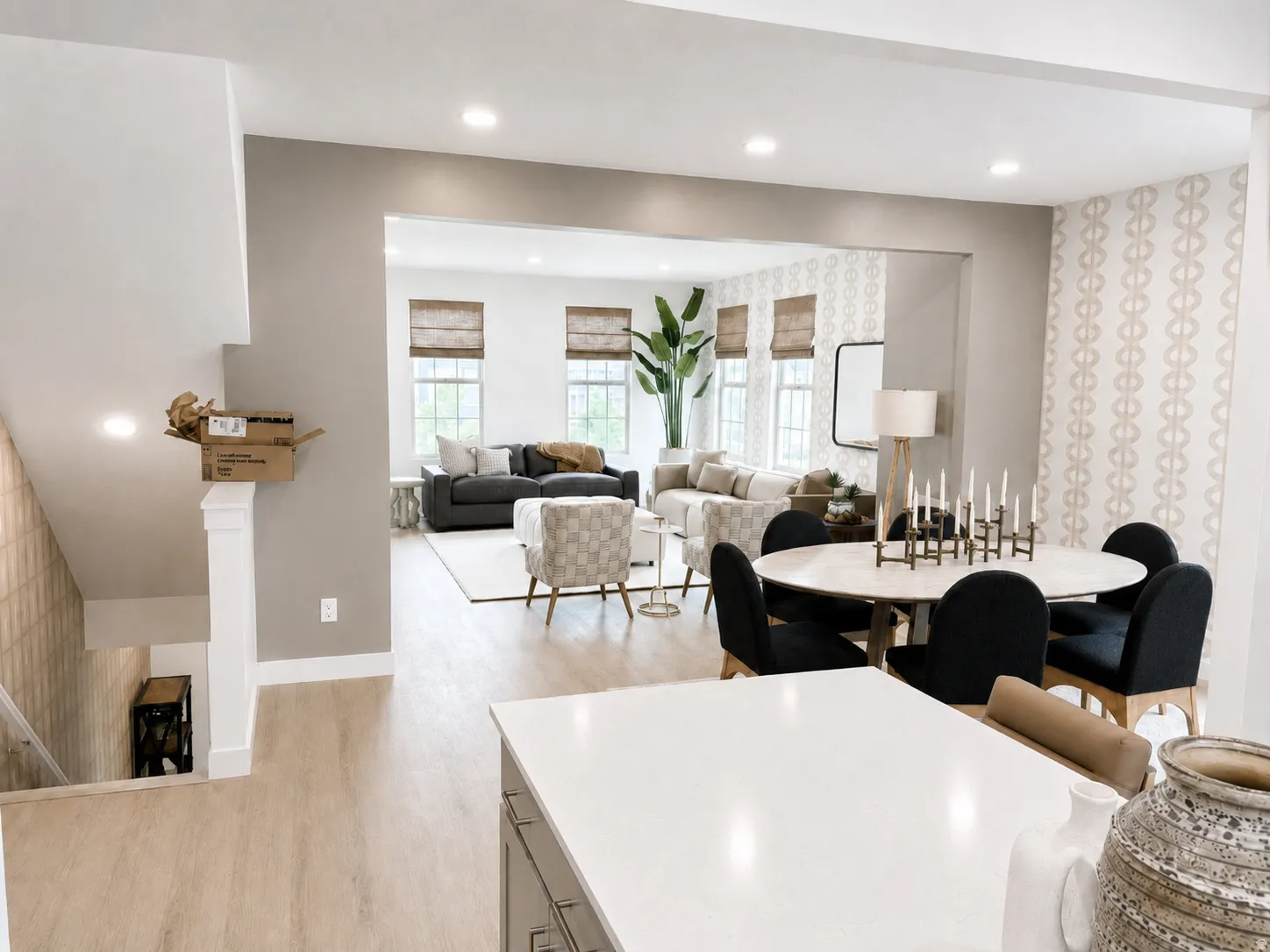 Recessed ceiling lighting, light wood-finish flooring, white kitchen countertop, white stair railing, and a dining area with patterned wallpaper