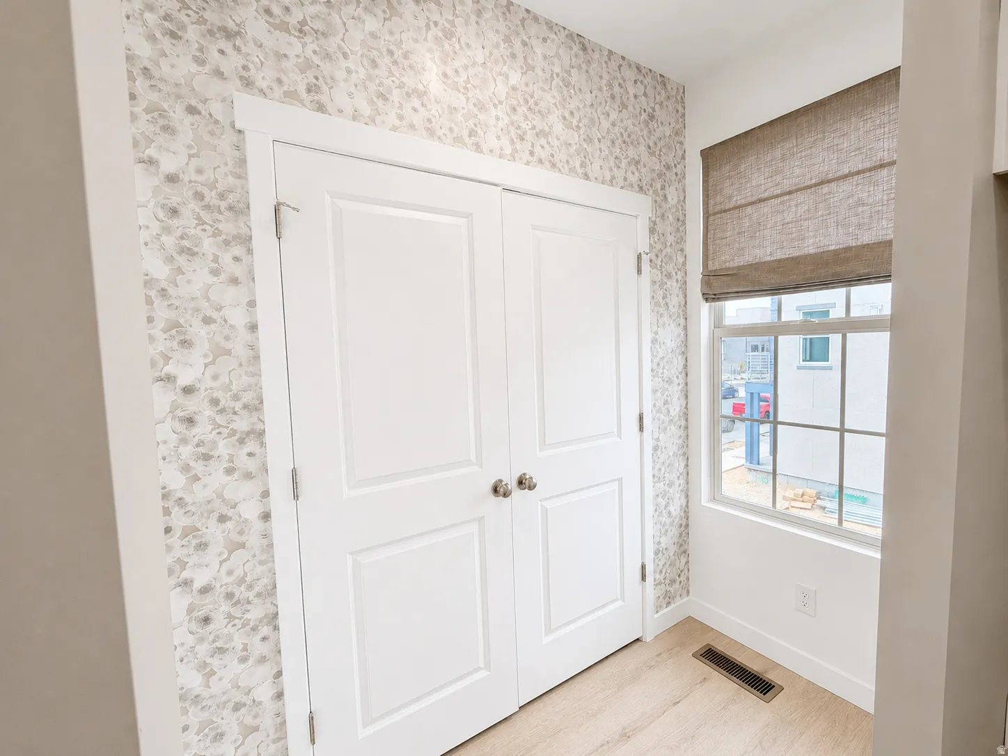 Patterned wall covering, paneled double doors, window with grid, wood-finish flooring, and a fabric Roman shade