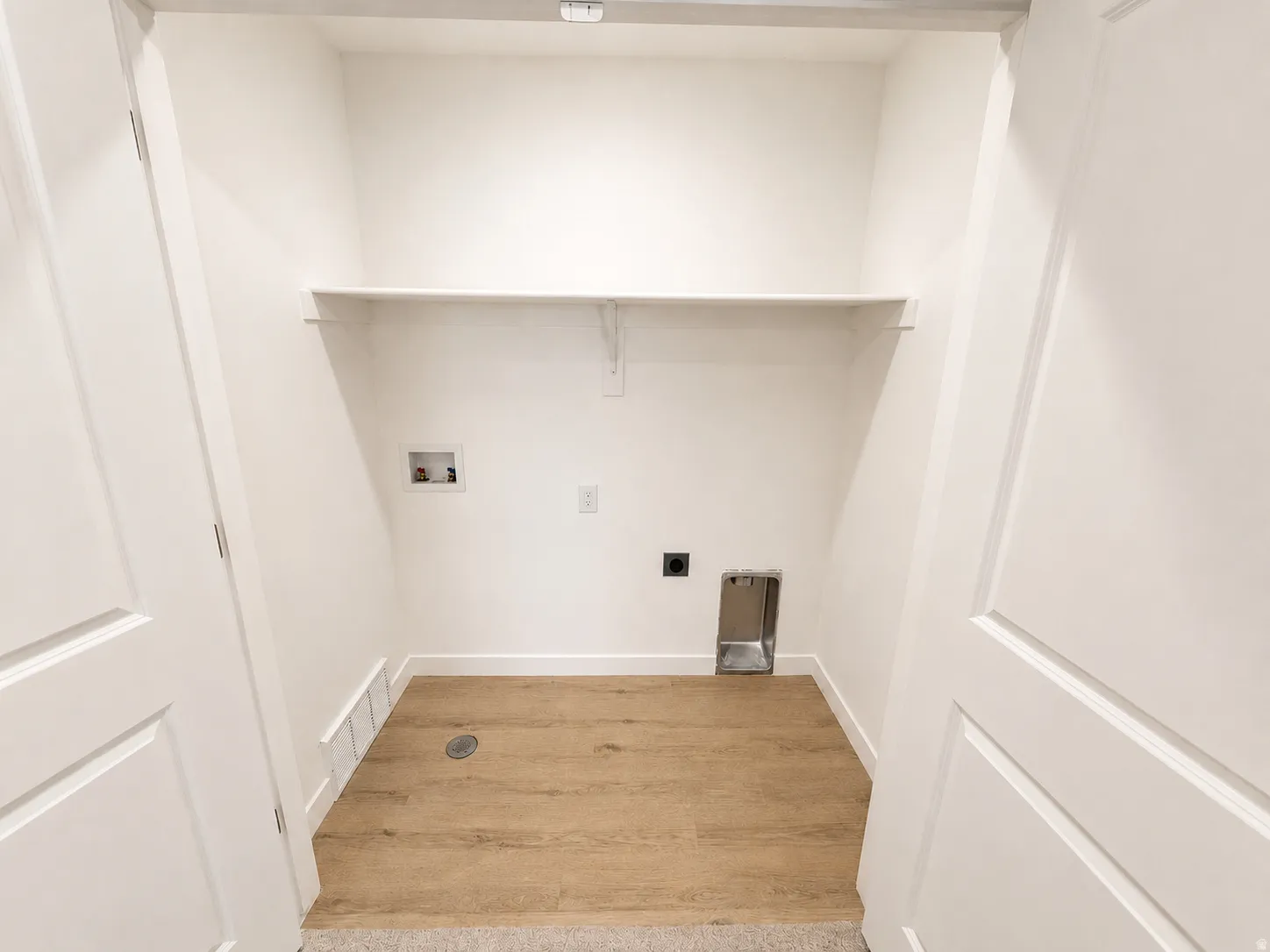 Dedicated utility space featuring a wall-mounted shelf, light wood-finish flooring, and white paneled doors