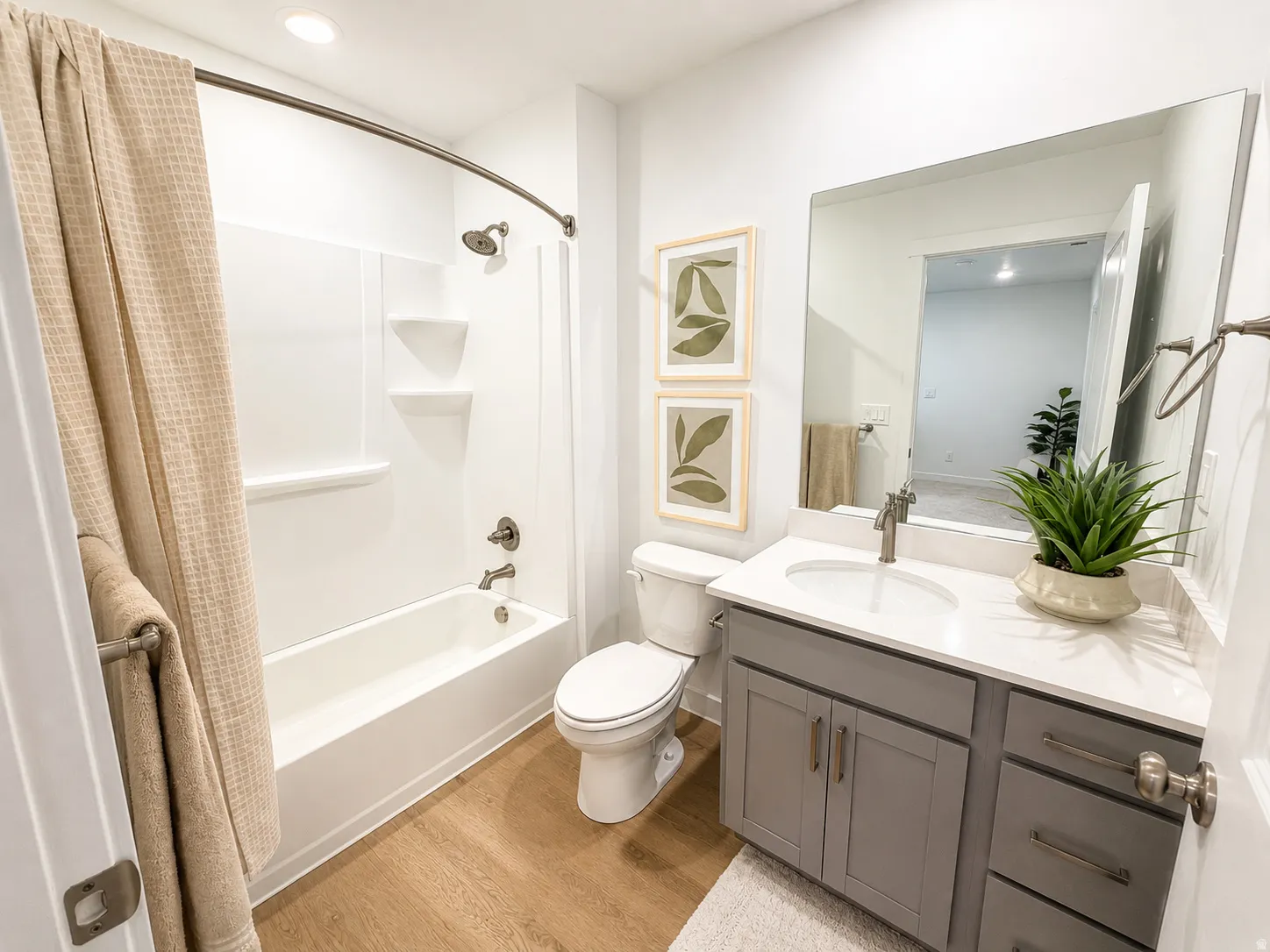 Bathroom featuring wood-finish flooring, a white vanity with a rectangular sink, a built-in tub with shower, and a curved shower rod