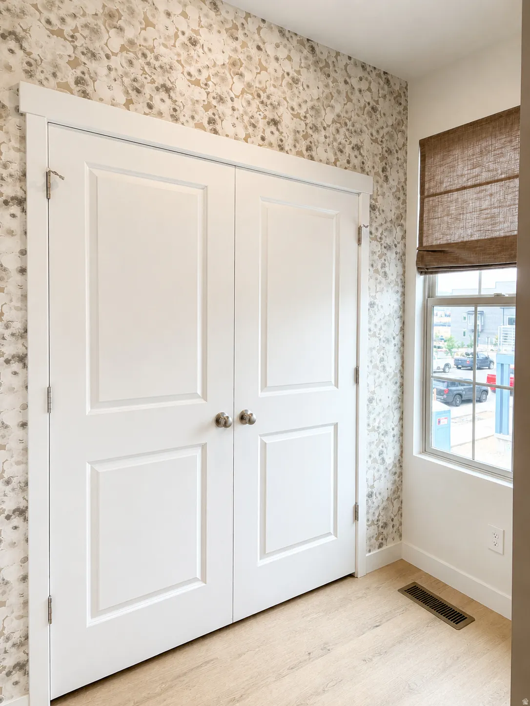 White panel doors with brushed nickel hardware, light wood-finish flooring, and a window with a woven Roman shade