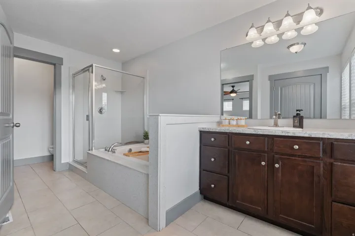 Spacious bathroom featuring a glass-enclosed shower, built-in soaking tub, tile flooring, and a vanity with a large mirror and wood-finish cabinetry