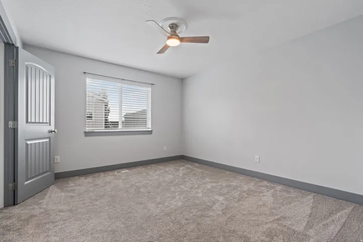 Spacious room featuring neutral paint, grey carpet flooring, a ceiling fan with light, and a window with blinds