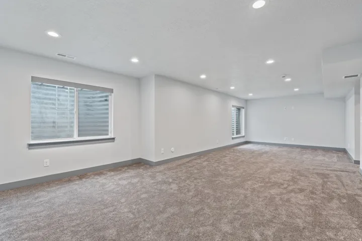 Spacious room with recessed lighting, light-toned carpeting, two windows, and neutral wall tones