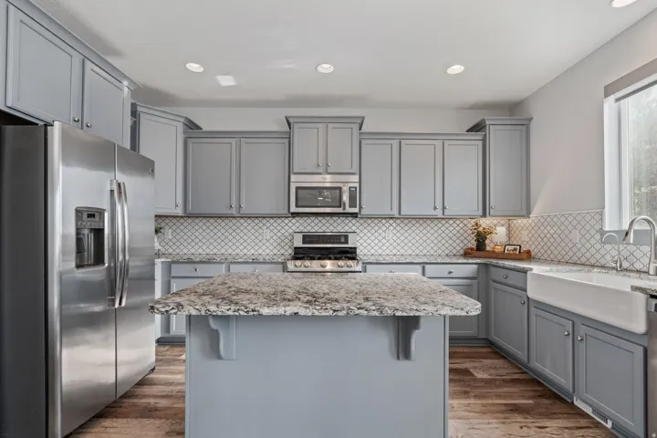 Kitchen featuring a central island with a stone countertop, grey cabinetry, stainless steel appliances, a white farmhouse sink, and wood-finish flooring