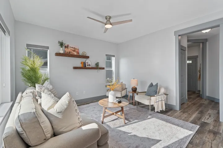 Spacious living area featuring light gray walls, wood-finish flooring, a ceiling fan with integrated lighting, and a doorway with gray trim