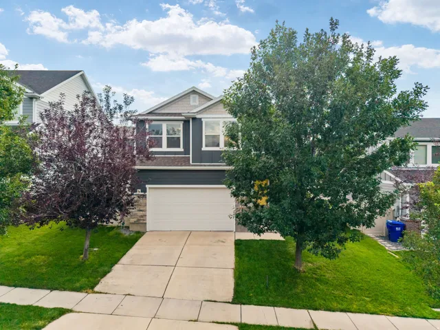 Two-story residence featuring a dark gray siding exterior, an attached garage, a paved driveway, and mature landscaping