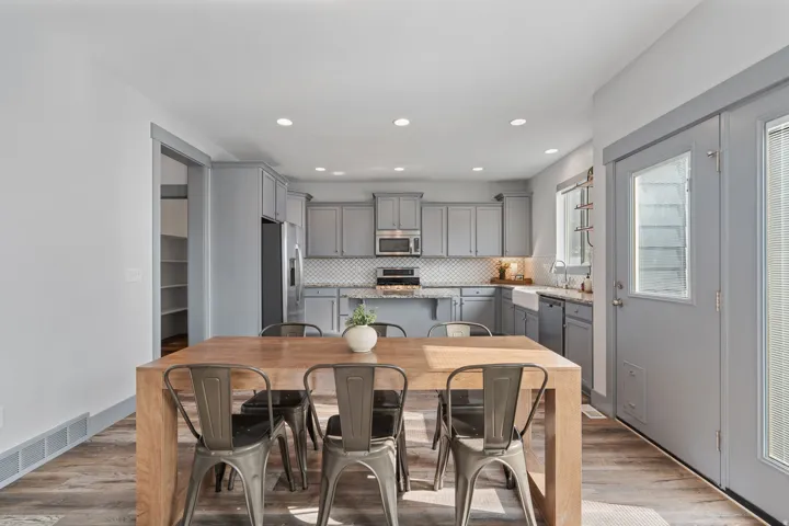 Kitchen featuring light gray cabinetry, stainless steel appliances, a white farmhouse sink, granite countertops, and a full tile backsplash