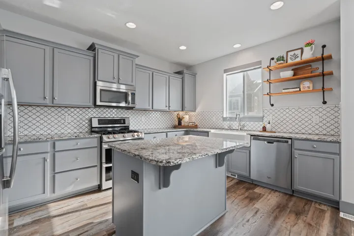 Kitchen featuring gray cabinetry, stainless steel appliances, granite countertops, wood-finish flooring, and a white farmhouse sink