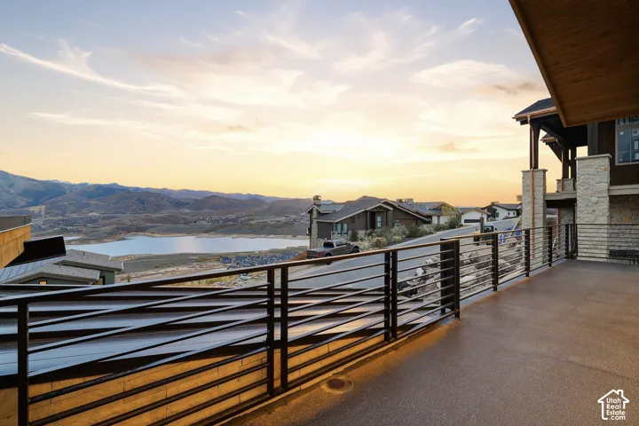 Covered deck featuring a concrete floor, metal railing, stone-clad structural pillars, and wood-paneled ceiling, overlooking mountain and water scenery