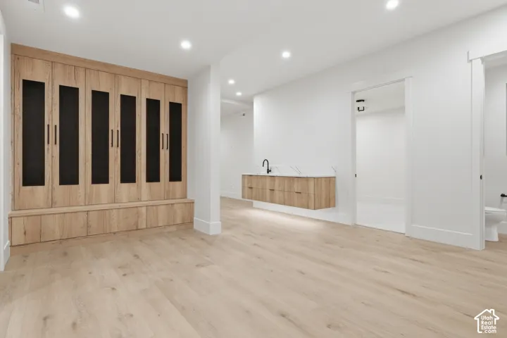 Floor-to-ceiling wood-finish built-in cabinetry with integrated bench seating, recessed lighting, wood-finish flooring, floating wall-mounted vanity with solid-surface countertop, and matte black plumbing fixtures